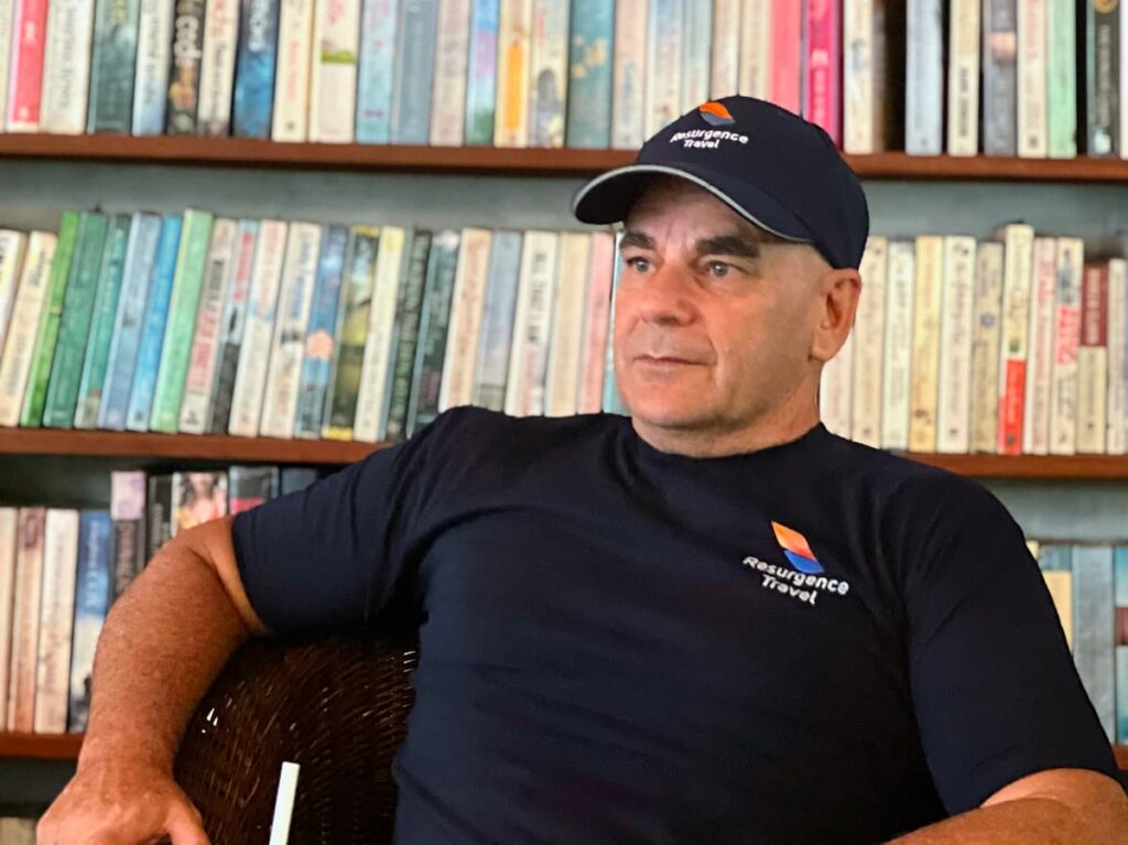 David Hibbins, Thailand-based travel publisher and founder of Resurgence Travel, seated in front of bookshelves
