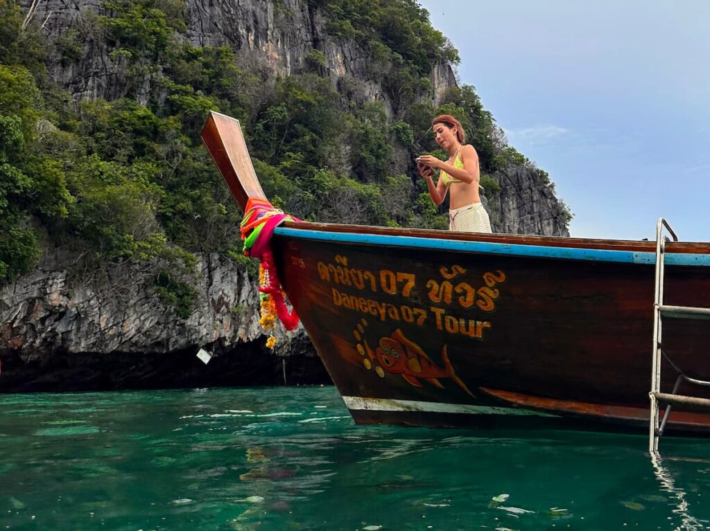 Traveller photographing a traditional longtail boat beside limestone cliffs in Thailand